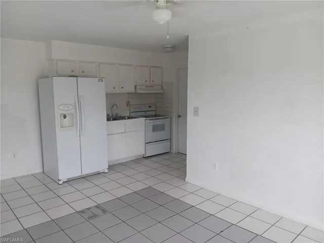Kitchen featuring white appliances, decorative backsplash, light countertops, under cabinet range hood, and light tile patterned floors