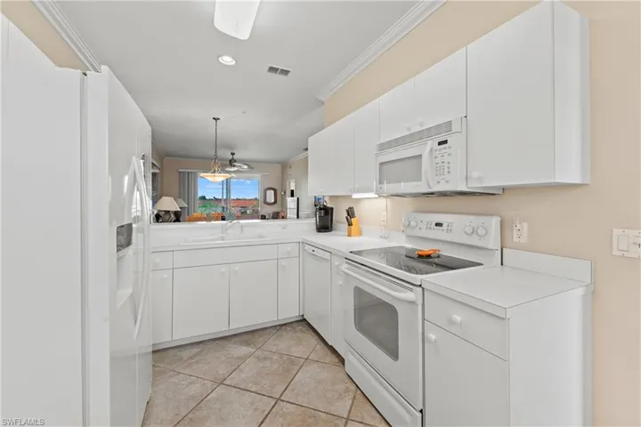 Kitchen featuring white appliances, crown molding, sink, light tile patterned flooring, and white cabinetry
