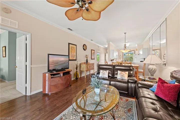 Living room with ornamental molding, ceiling fan, and dark wood-type flooring