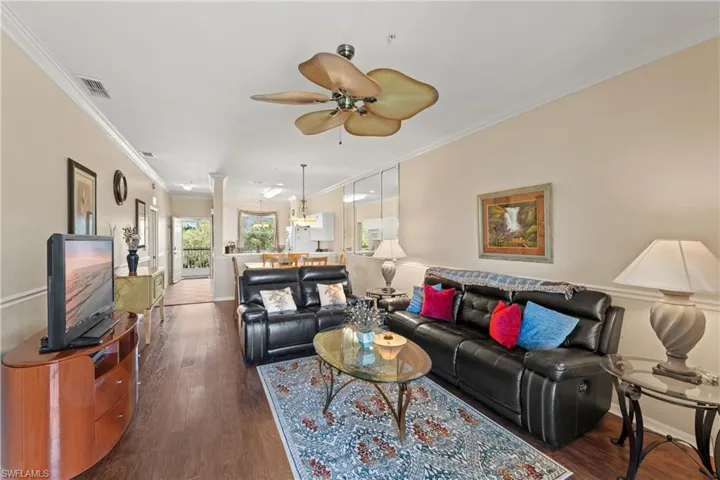Living room featuring ceiling fan, crown molding, and dark wood-type flooring