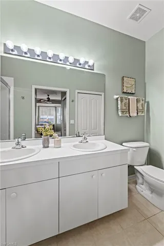 Bathroom featuring ceiling fan, tile patterned flooring, an enclosed shower, toilet, and vanity