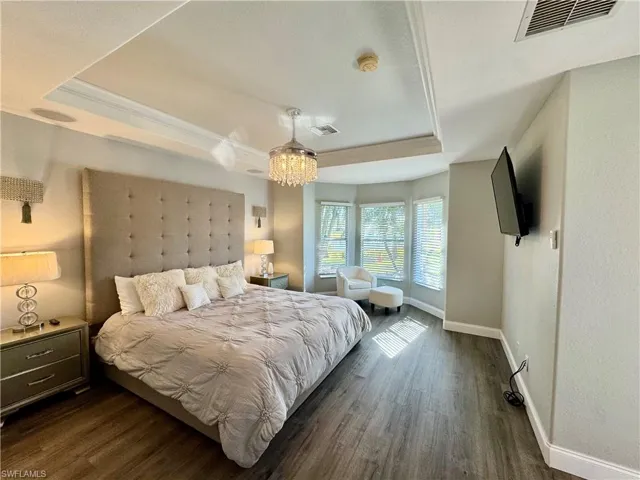 Bedroom with a chandelier, dark hardwood / wood-style flooring, ornamental molding, and a tray ceiling
