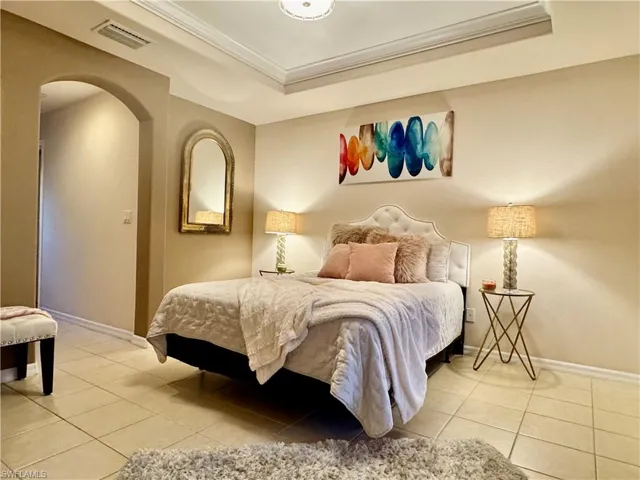 Bedroom featuring light tile patterned flooring, ornamental molding, and a tray ceiling