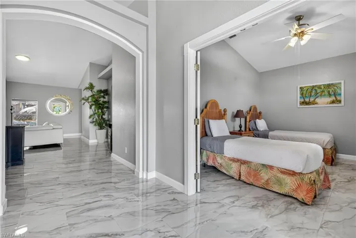Bedroom featuring arched walkways, lofted ceiling, light marble finish flooring, and a ceiling fan