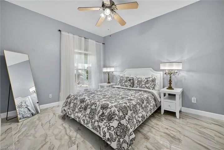 Bedroom featuring light marble finish flooring, ceiling fan, and a textured wall