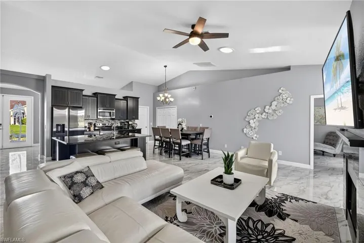 Living room with a chandelier, ceiling fan, light marble finish flooring, vaulted ceiling, and recessed lighting