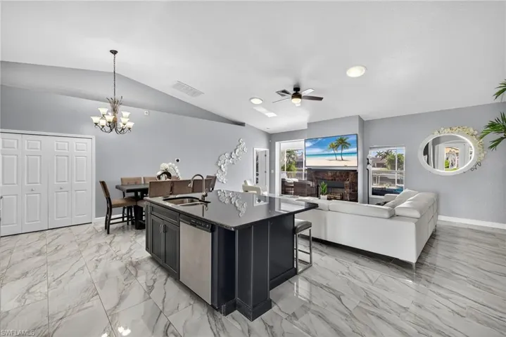Kitchen featuring open floor plan, pendant lighting, dark cabinetry, a center island with sink, and stainless steel dishwasher