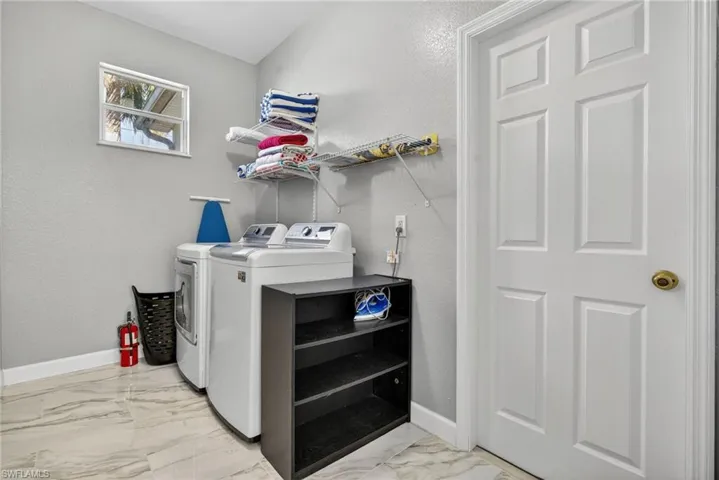 Laundry area featuring a textured wall, light marble finish flooring, and washing machine and dryer