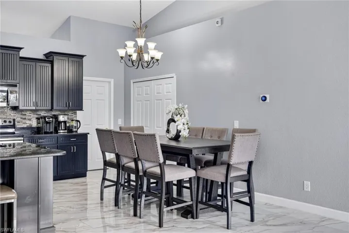 Dining room featuring light marble finish floors, a chandelier, and high vaulted ceiling