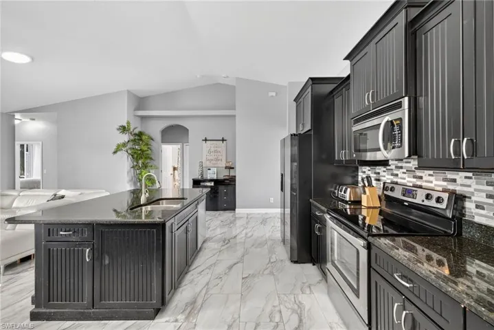 Kitchen with stainless steel appliances, open floor plan, dark cabinets, dark stone counters, and decorative backsplash