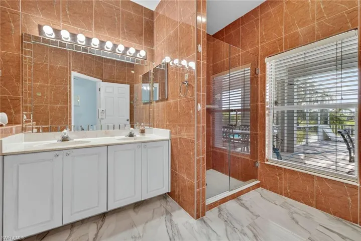 Bathroom featuring tile walls, double vanity, a stall shower, and light marble finish floors