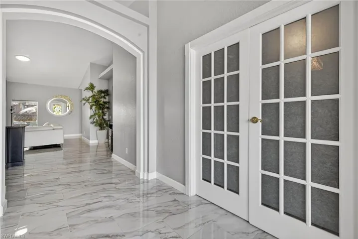 Corridor with arched walkways, marble tiled flooring, and lofted ceiling