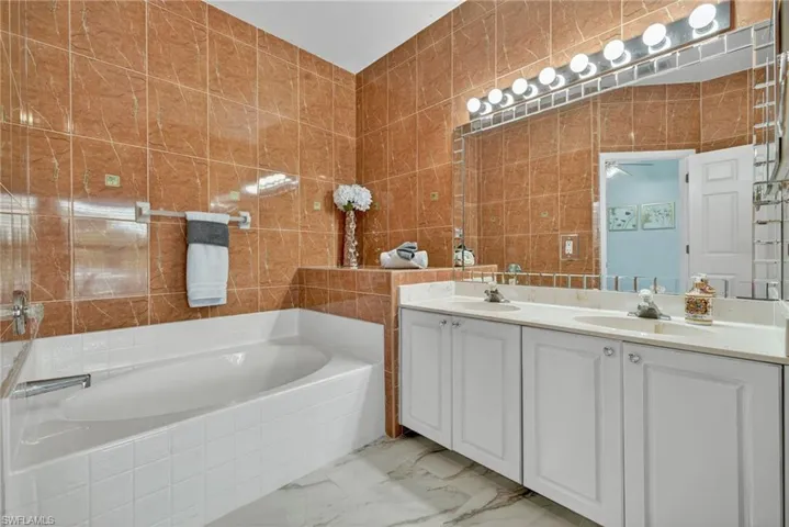 Full bath featuring tile walls, a garden tub, double vanity, and light marble finish flooring