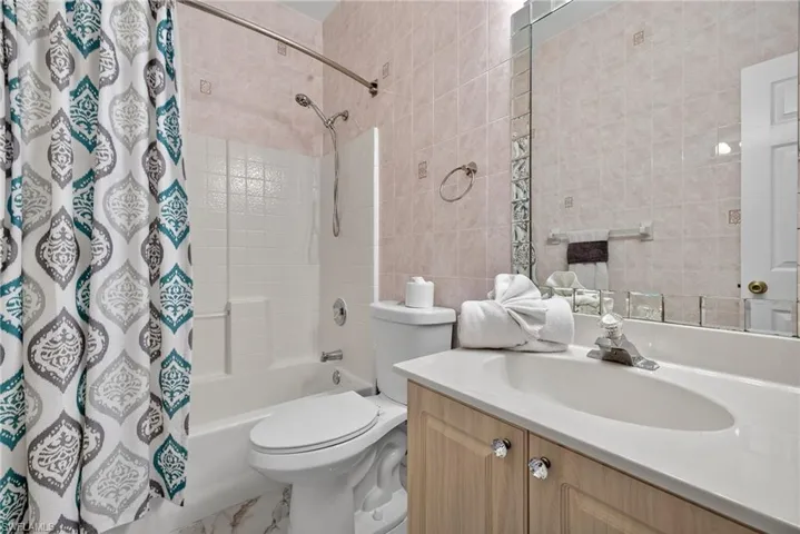 Bathroom featuring tile walls, shower / bath combination with curtain, and vanity