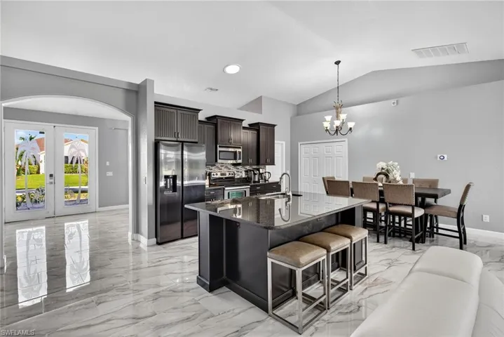 Kitchen featuring light marble finish flooring, stainless steel appliances, a kitchen breakfast bar, french doors, and dark stone countertops