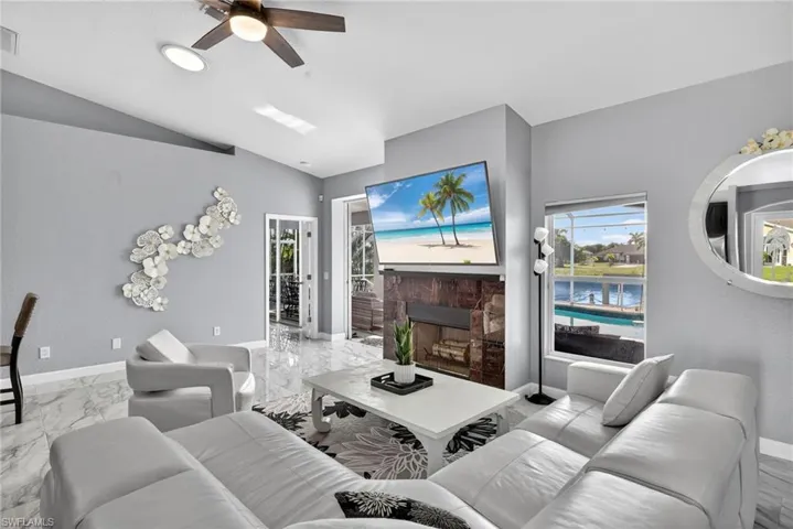 Living area featuring healthy amount of natural light, a stone fireplace, lofted ceiling, marble finish floors, and ceiling fan