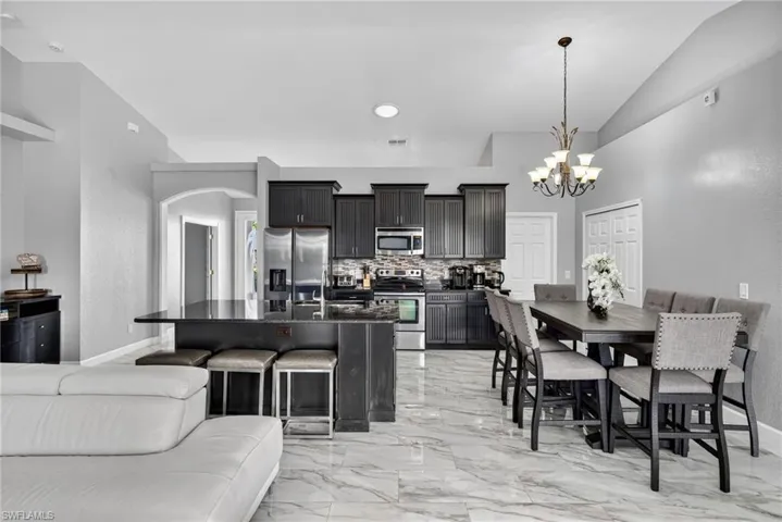 Kitchen with stainless steel appliances, open floor plan, light marble finish floors, decorative backsplash, and hanging light fixtures