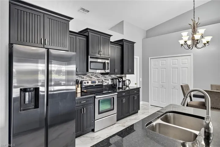 Kitchen featuring appliances with stainless steel finishes, light marble finish floors, decorative backsplash, hanging light fixtures, and dark cabinets