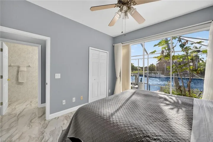 Bedroom featuring a water view, access to exterior, marble look tiles, a closet, and a ceiling fan