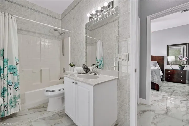 Ensuite bathroom with tile walls, shower / bath combo with shower curtain, vanity, and light marble finish floors