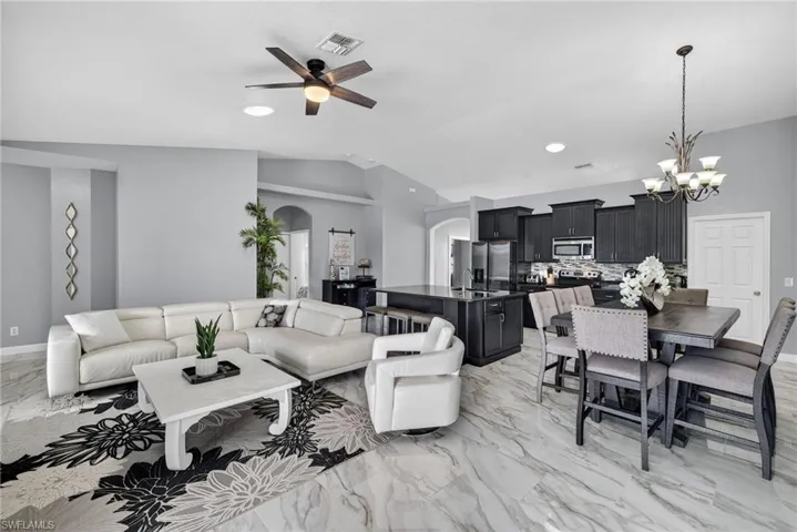 Living room featuring light marble finish floors, arched walkways, lofted ceiling, a chandelier, and ceiling fan