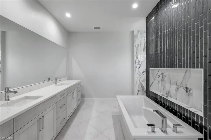 Bathroom featuring dual bowl vanity, tile flooring, and a bath to relax in