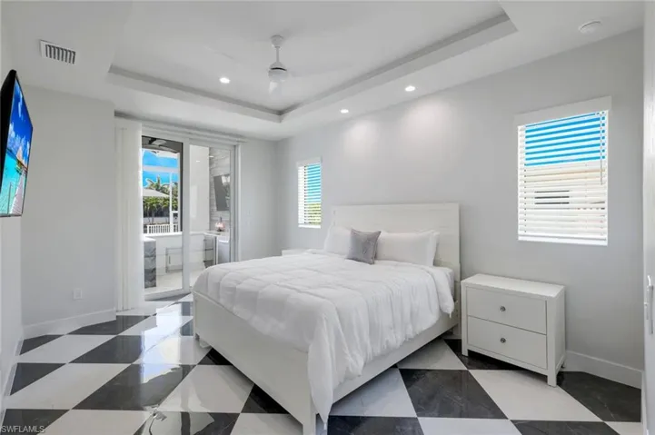 Tiled bedroom featuring ceiling fan, a tray ceiling, and access to exterior