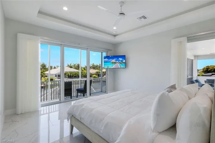 Tiled bedroom featuring ceiling fan, a raised ceiling, and access to outside