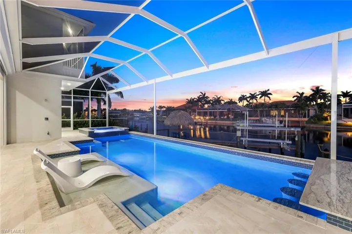 Pool at dusk featuring a patio area, glass enclosure, and an in ground hot tub