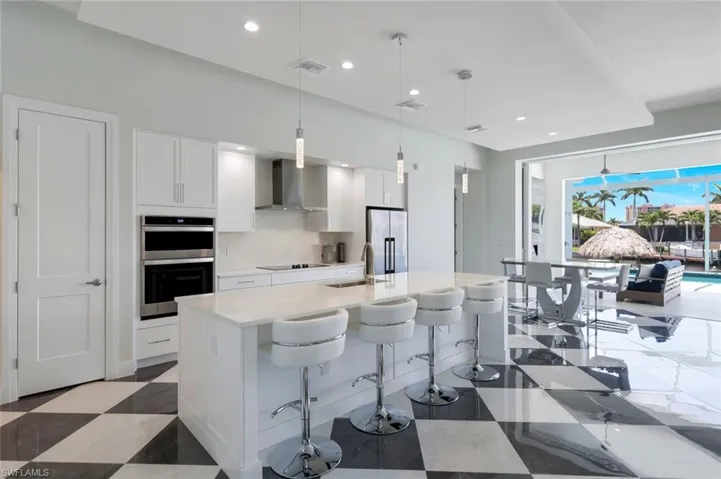 Kitchen featuring decorative light fixtures, wall chimney exhaust hood, stainless steel appliances, and white cabinets