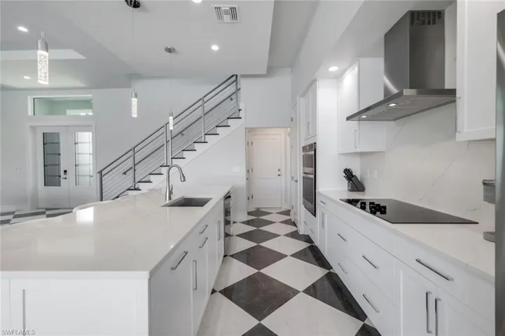 Kitchen featuring stainless steel appliances, hanging light fixtures, wall chimney exhaust hood, white cabinets, and sink