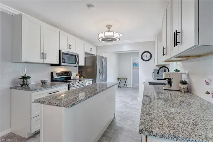 Kitchen featuring white cabinets, light stone countertops, appliances with stainless steel finishes, and baseboards