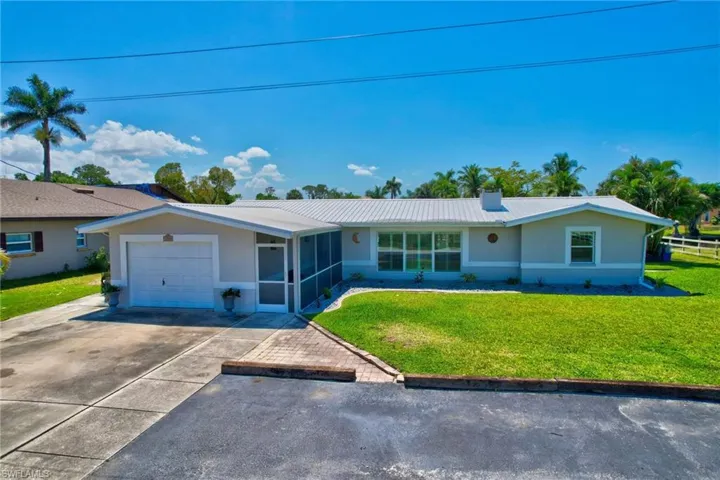 Ranch-style home featuring a sunroom, concrete driveway, metal roof, an attached garage, and a front lawn