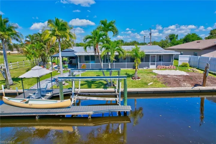 View of dock with a lawn, a water view, fence, and boat lift