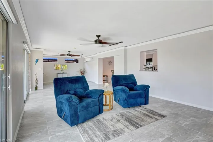 Living room with a wall mounted air conditioner, ceiling fan, baseboards, and crown molding