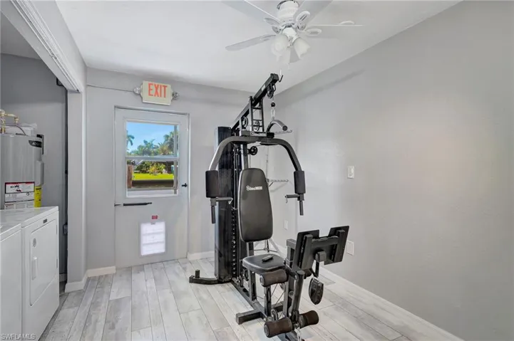 Exercise area with electric water heater, light wood-style flooring, independent washer and dryer, baseboards, and a ceiling fan