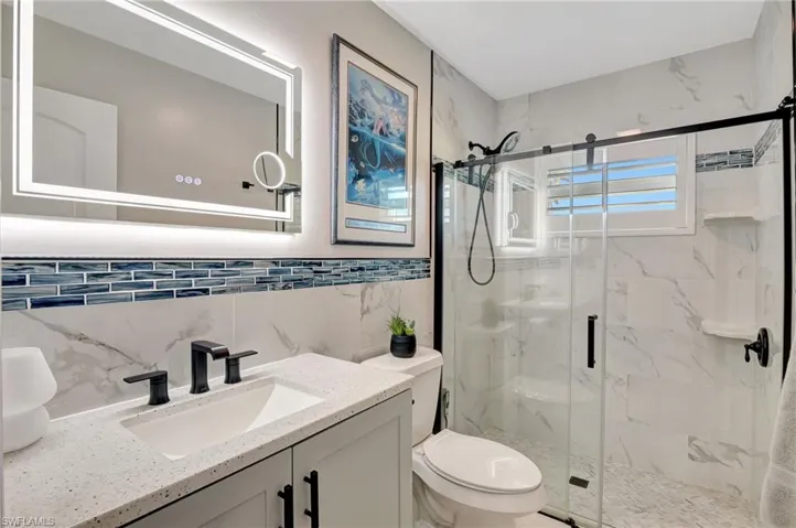 Bathroom with tile walls, a marble finish shower, toilet, and vanity