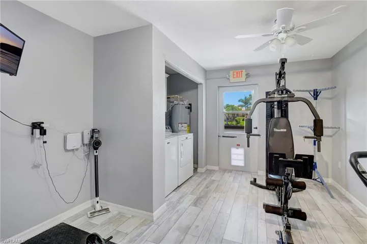 Exercise room with light wood-style flooring, baseboards, ceiling fan, electric water heater, and separate washer and dryer