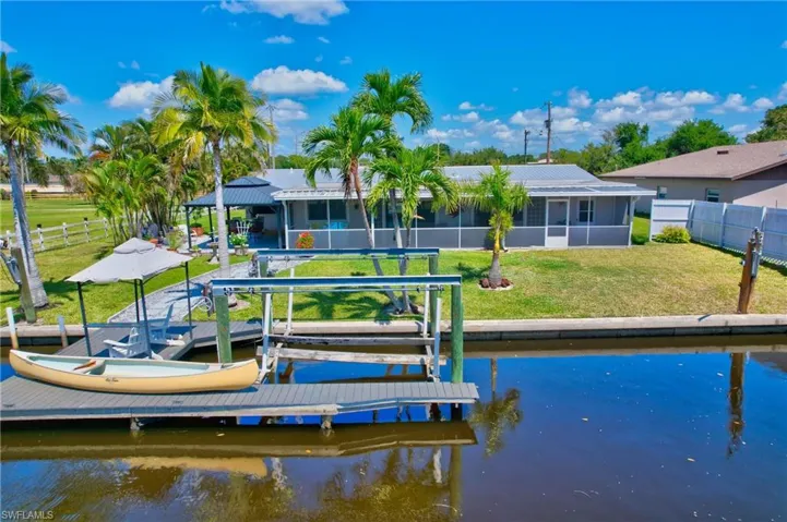 View of dock with boat lift, a fenced backyard, a water view, and a lawn