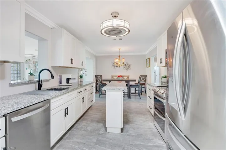 Kitchen with crown molding, a chandelier, a sink, white cabinets, and appliances with stainless steel finishes