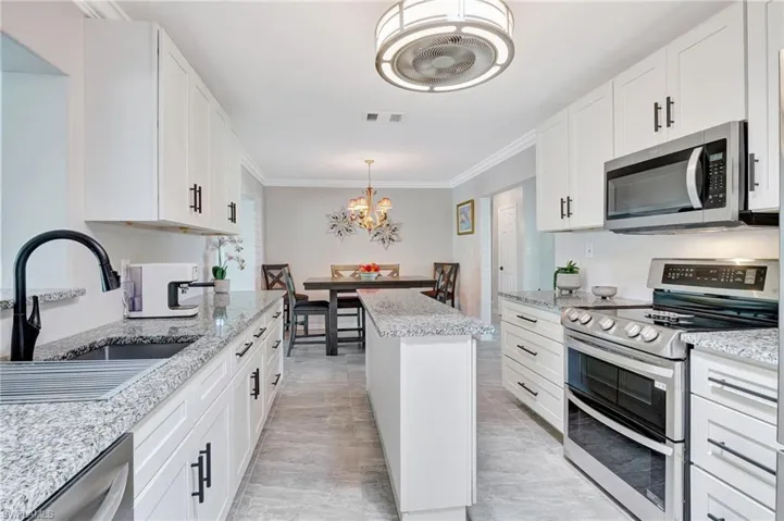 Kitchen with ornamental molding, stainless steel appliances, a chandelier, a sink, and visible vents