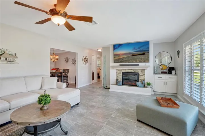 Living room with baseboards, a fireplace, visible vents, and ceiling fan with notable chandelier