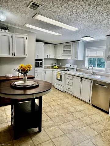 Kitchen with white cabinets, electric stove, light countertops, stainless steel dishwasher, and a textured ceiling