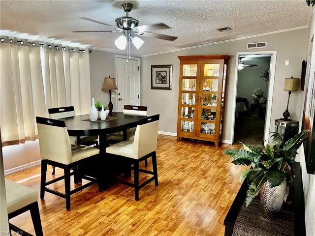 Dining room featuring a textured ceiling, crown molding, light wood finished floors, a ceiling fan