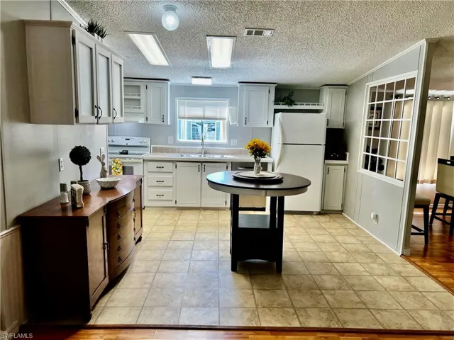 Kitchen featuring white appliances, light countertops, a textured ceiling, open shelves, and white cabinetry