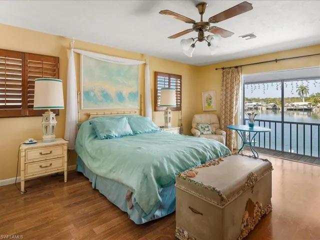 Bedroom with a water view, dark hardwood / wood-style floors, access to exterior, and ceiling fan