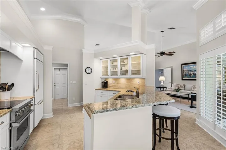 Kitchen featuring crown molding, glass insert cabinets, light stone countertops, a peninsula, and high quality appliances