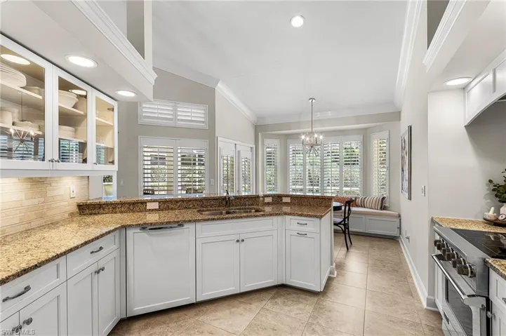 Kitchen with white cabinetry, crown molding, high end range, light stone counters, and glass insert cabinets