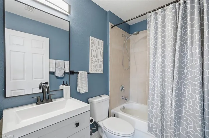 Bathroom featuring a white vanity with integrated sink, black hardware, a framed mirror, and a tub/shower combination with light-toned wall tile