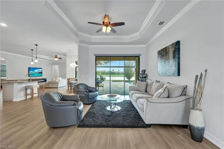 Living area featuring ceiling fan, light wood-style flooring, ornamental molding, a tray ceiling, and arched walkways